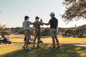 Three men in golf attire toasting with drinks on a sunny golf course
